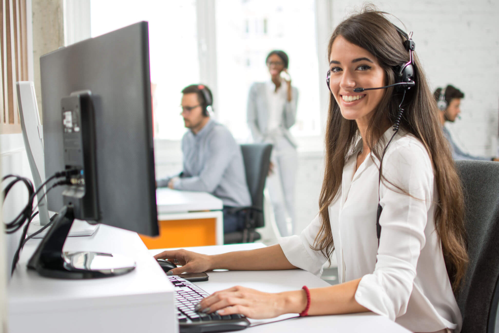 How can I help you? Beautiful call center workers in headphones are working at modern office.