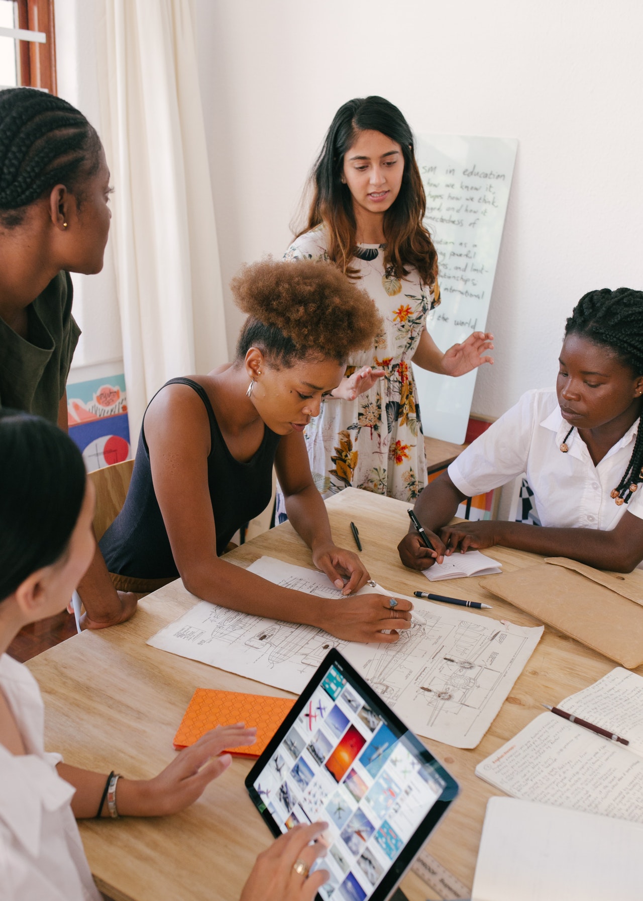 Five women in a professional setting collaboratively discussing a paper chart