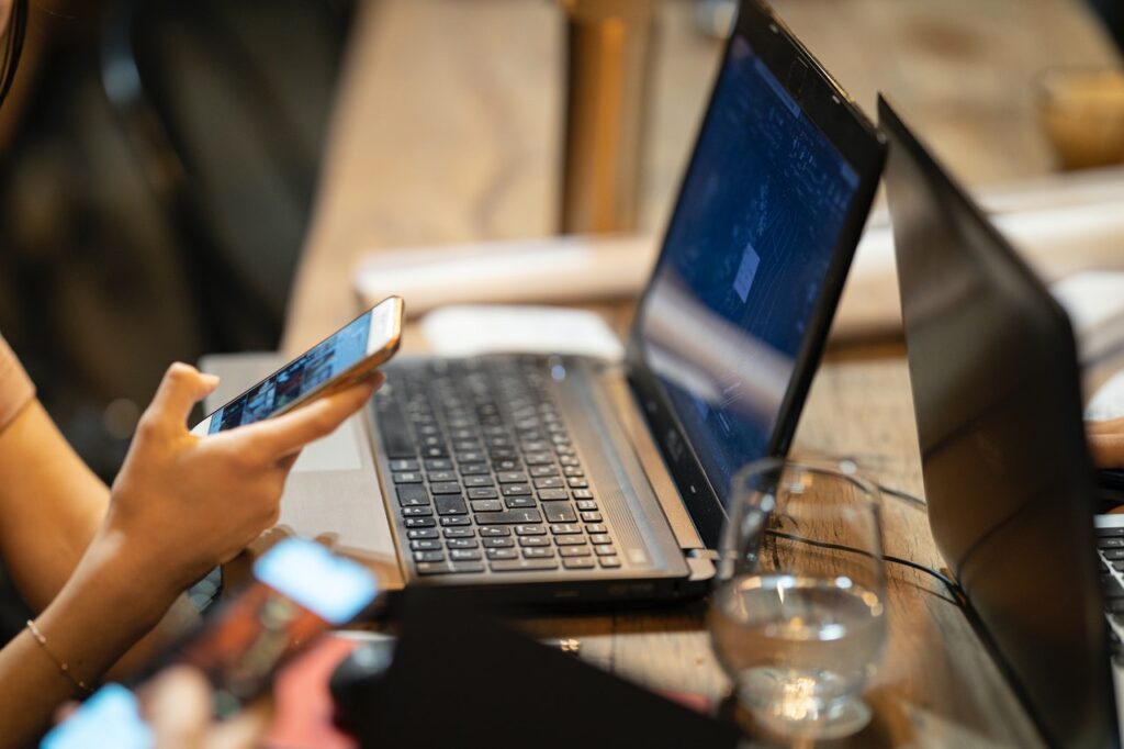 A woman's hand scrolling through a smartphone, with a laptop open in front of her