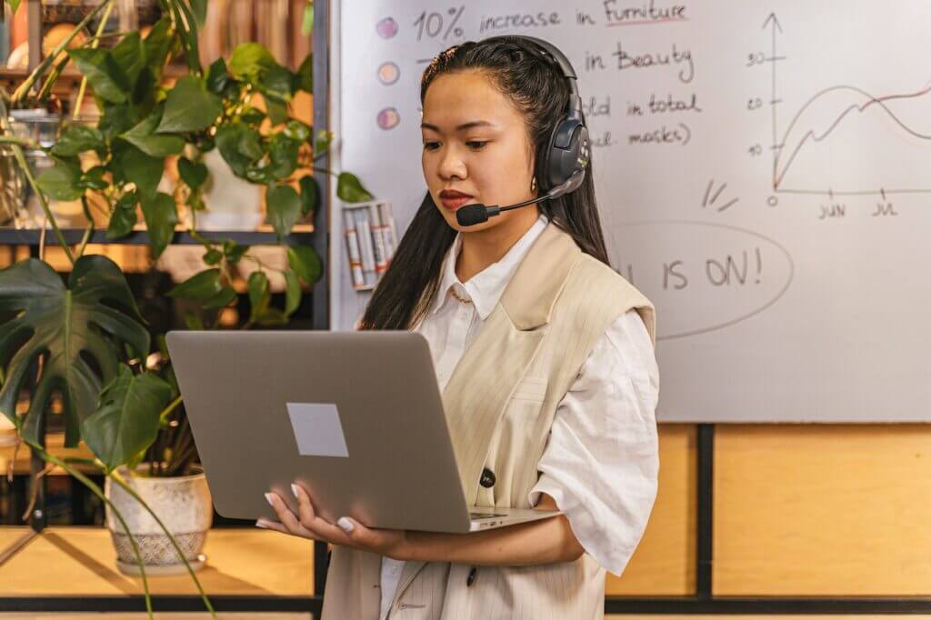 A contact center agent with a headset, looking at the laptop she is holding