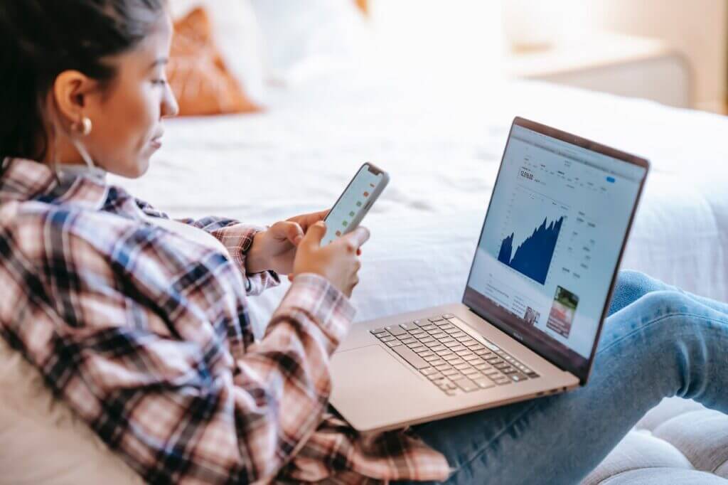 A woman browsing on her phone while simultaneously working on a laptop resting on her lap