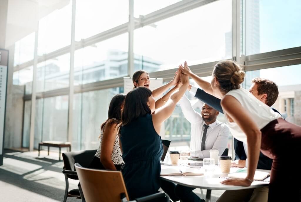 Six managers doing a group high five in an office