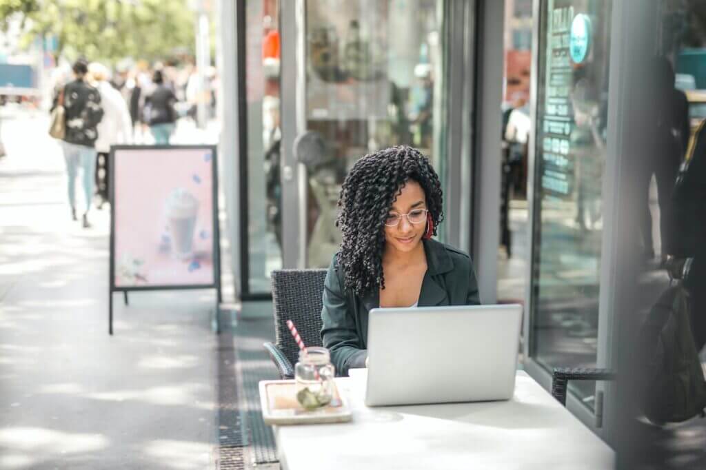 Focused woman using a laptop at an outdoor street café, possibly working or browsing the internet.