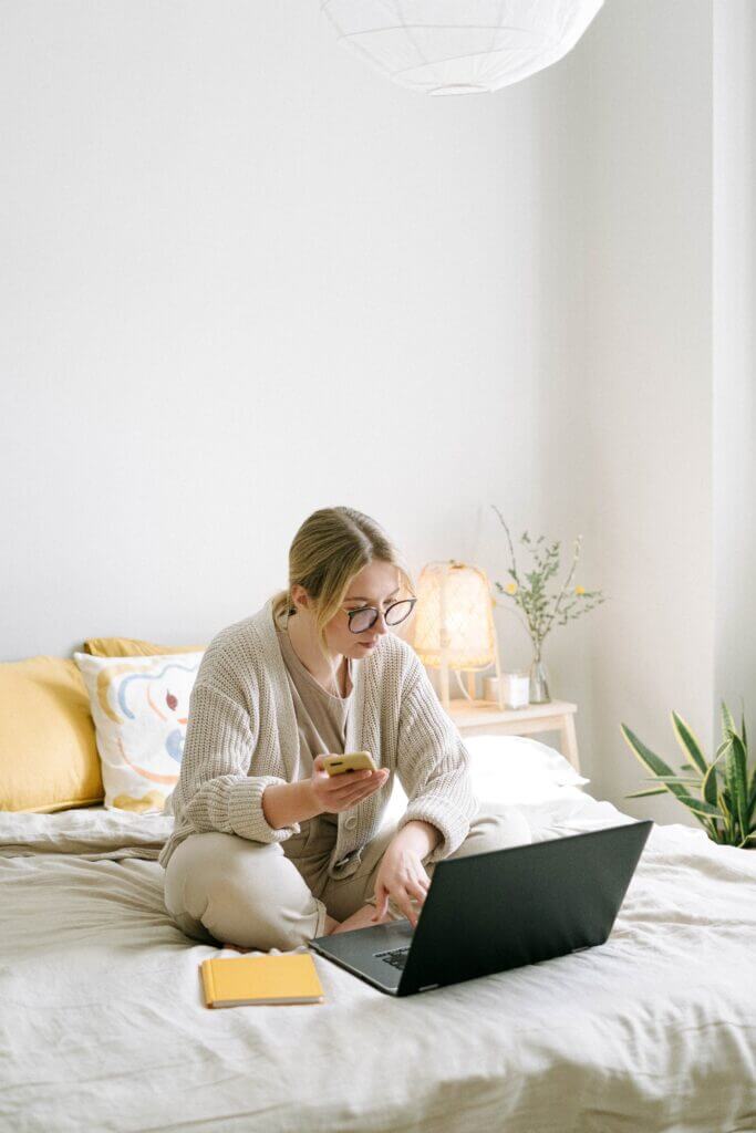 Woman multitasking in bed with a laptop and a mobile phone in her hands