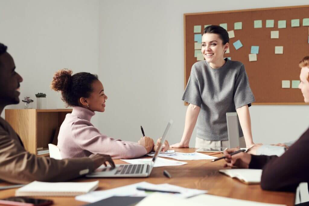 Group of People Seated Around a Table in an Office, with One Person Presenting Information on a board