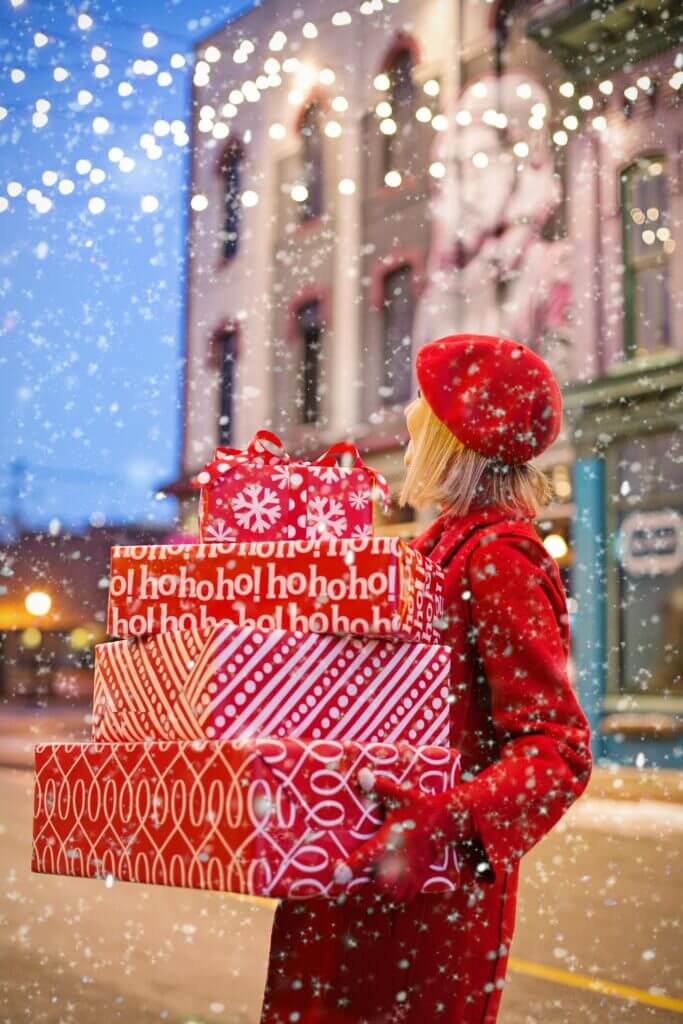 Woman on a snowy street holding wrapped gifts.