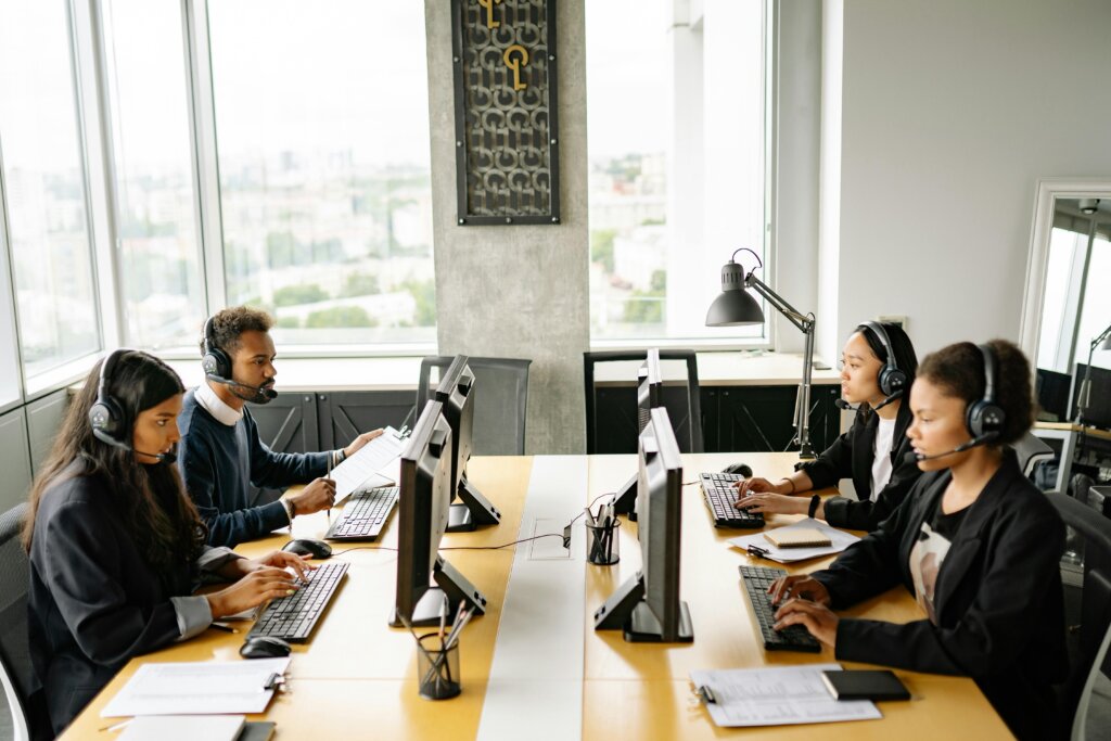An office scene featuring four Customer Support Representatives with headsets working at their desks.