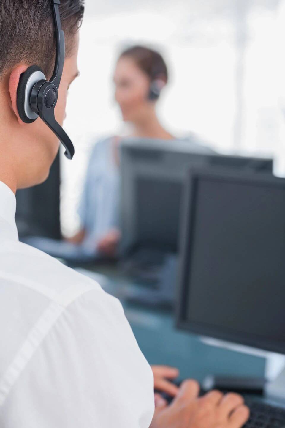 Call center agent sitting at his work desk with headset on, focusing on a computer screen.