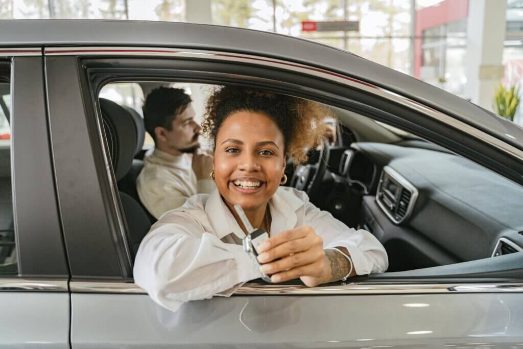 Smiling Woman Sitting in a New Car at the Car Salon and Showing Car Keys
