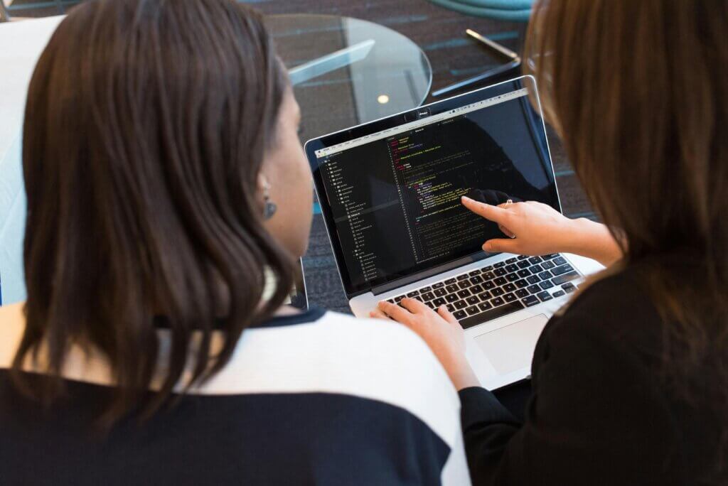 Two Women Looking at the Code at Laptop
